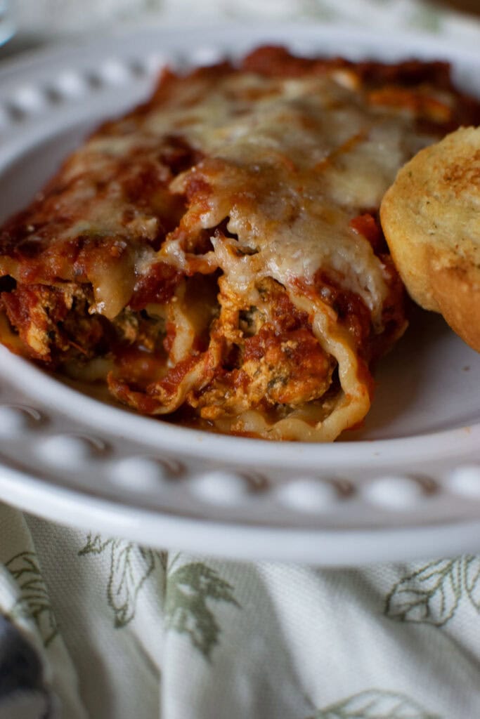 Two spinach and chicken manicotti served on a white dinner plate with a side of garlic bread.