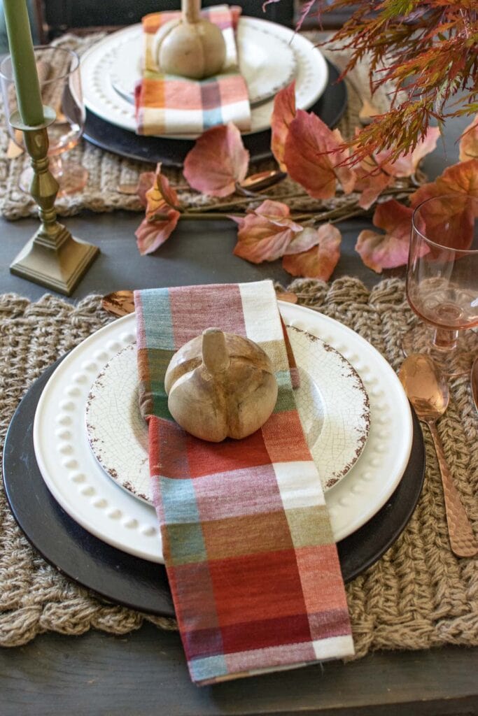 A cozy autumn dinner table plate stack with wood charger plates, white dinner plates and faux crackle salad plates. All topped with a plaid napkin.