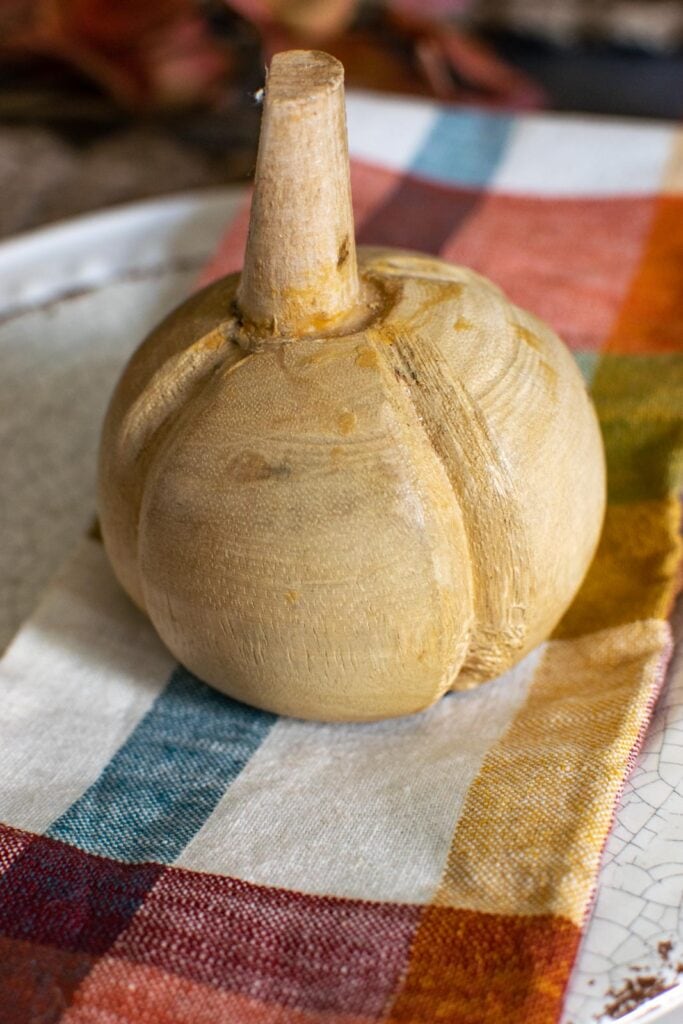 A hand carved wood pumpkin sitting on top of a plaid napkin on a fall dinner table.