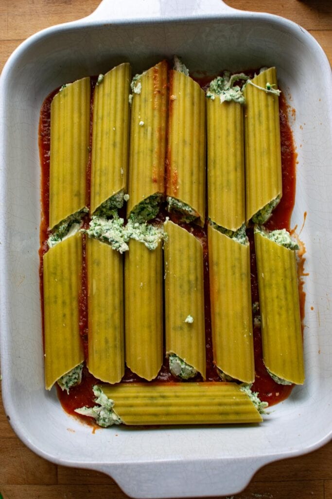 manicotti shells stuffed with a cheesy chicken and spinach mixture placed on top of marina sauce in a casserole dish.