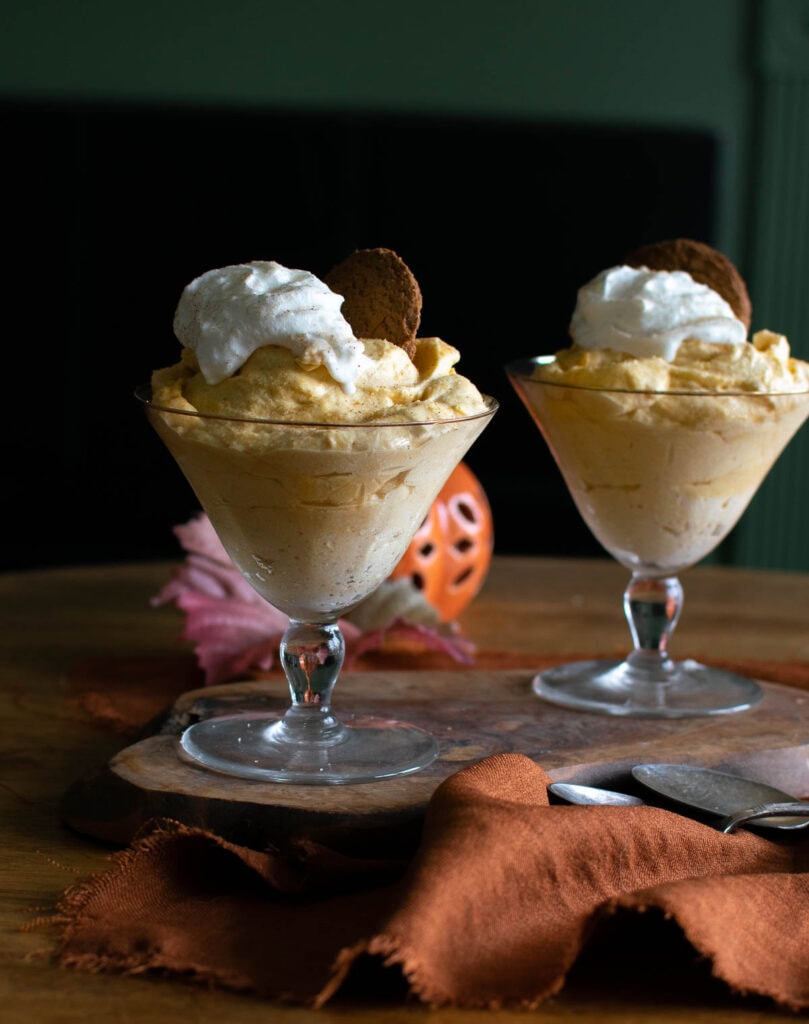 Two dessert cups filled with pumpkin mousse, whipped cream and a ginger cookie.
