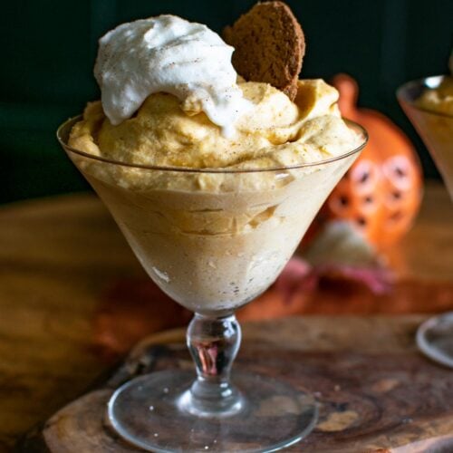 A footed dessert bowl filled with pumpkin mousse topped with whipped cream and a gingersnap cookie.