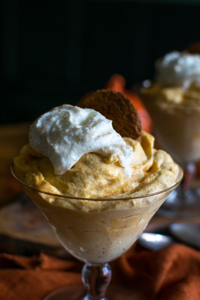 A footed dessert cup with pumpkin mousse topped with whipped cream and a ginger cookie.