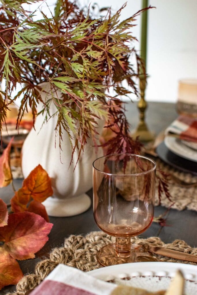 Japanese maple branches in a rustic water jug on a table decorated for fall.