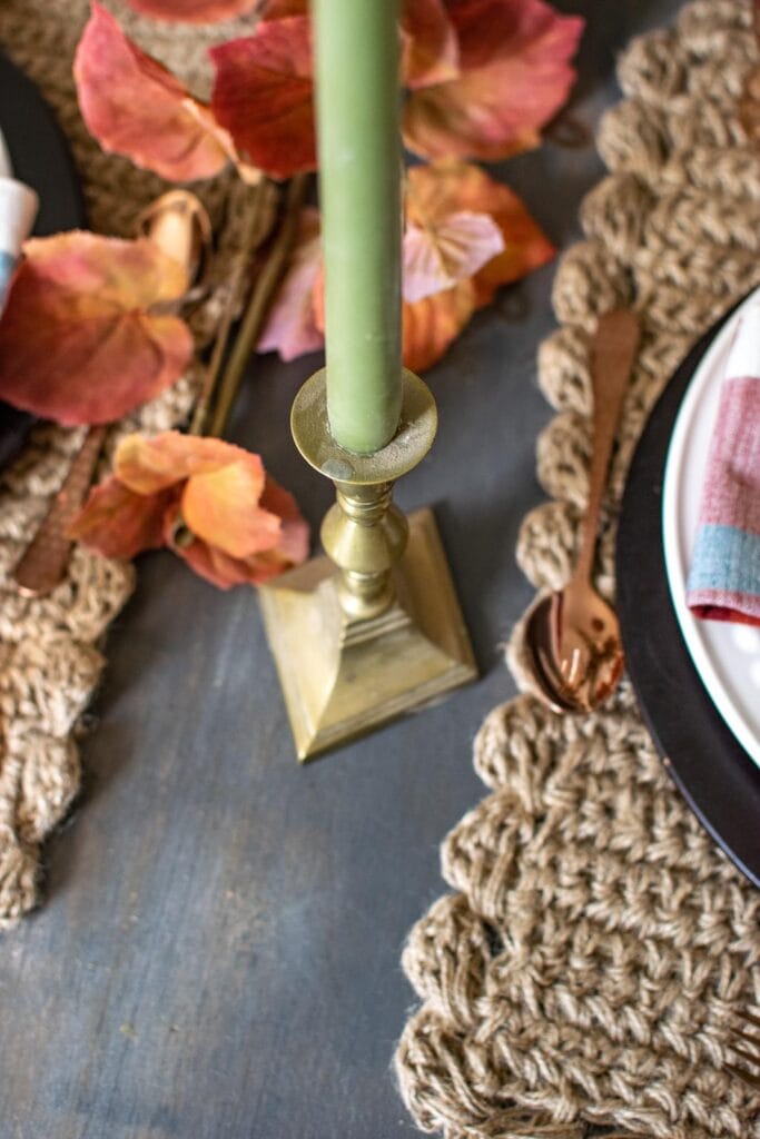 Brass candlesticks with green taper candles on a dinner table set for fall.