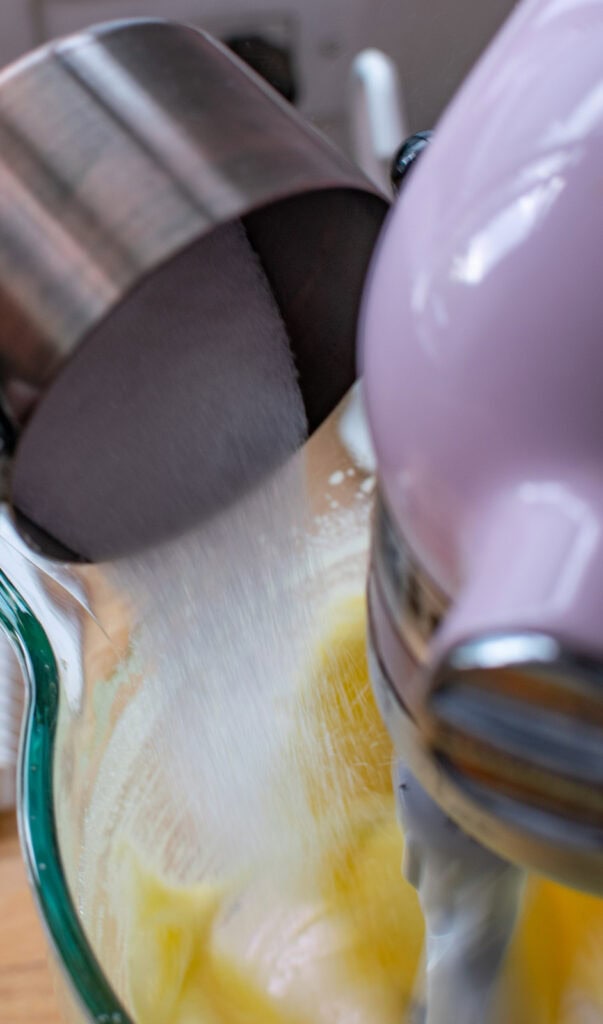 Sugar slowly being poured into the beaten eggs in a stand mixer.