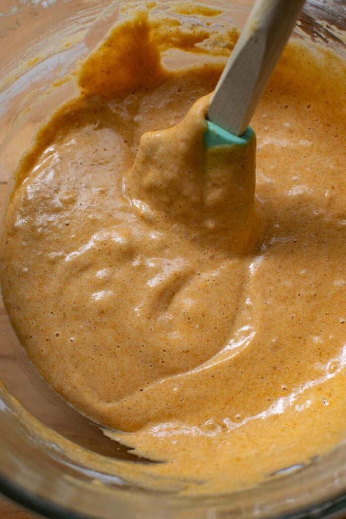 Flour and spice mixture folded into the egg and pumpkin mixture in a glass mixing bowl, using a rubber spatula.
