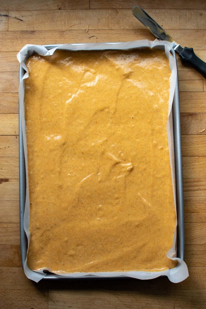Pumpkin sponge cake in a jelly roll pan that is lined with parchment paper.