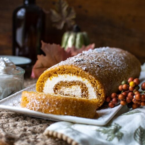 A pumpkin roll cake filled with cream cheese filling on a white serving plate.