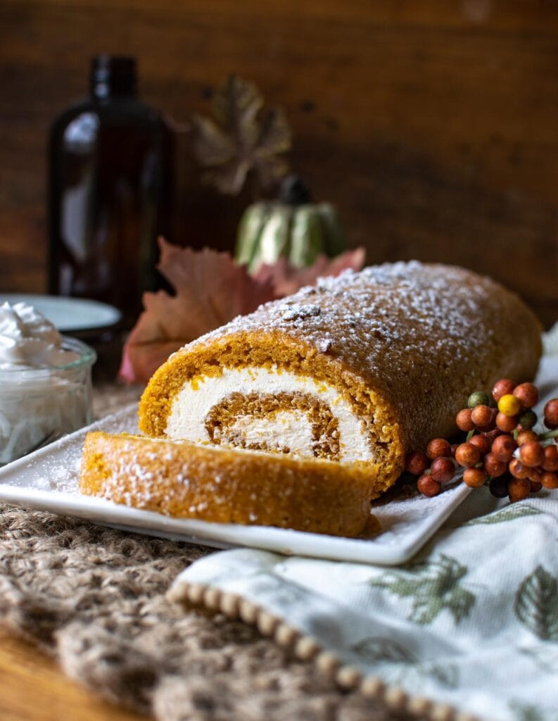 A pumpkin roll cake filled with cream cheese filling on a white serving plate.
