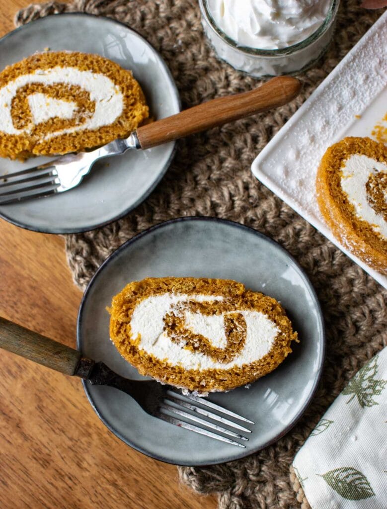Slices of pumpkin roll cake with a fluffy cream cheese filling on grey dessert plates.