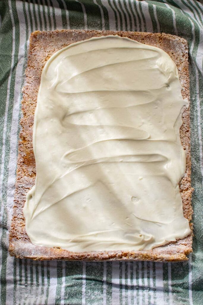 Cream cheese filling spread out over a pumpkin sponge cake before rolling it into a log.