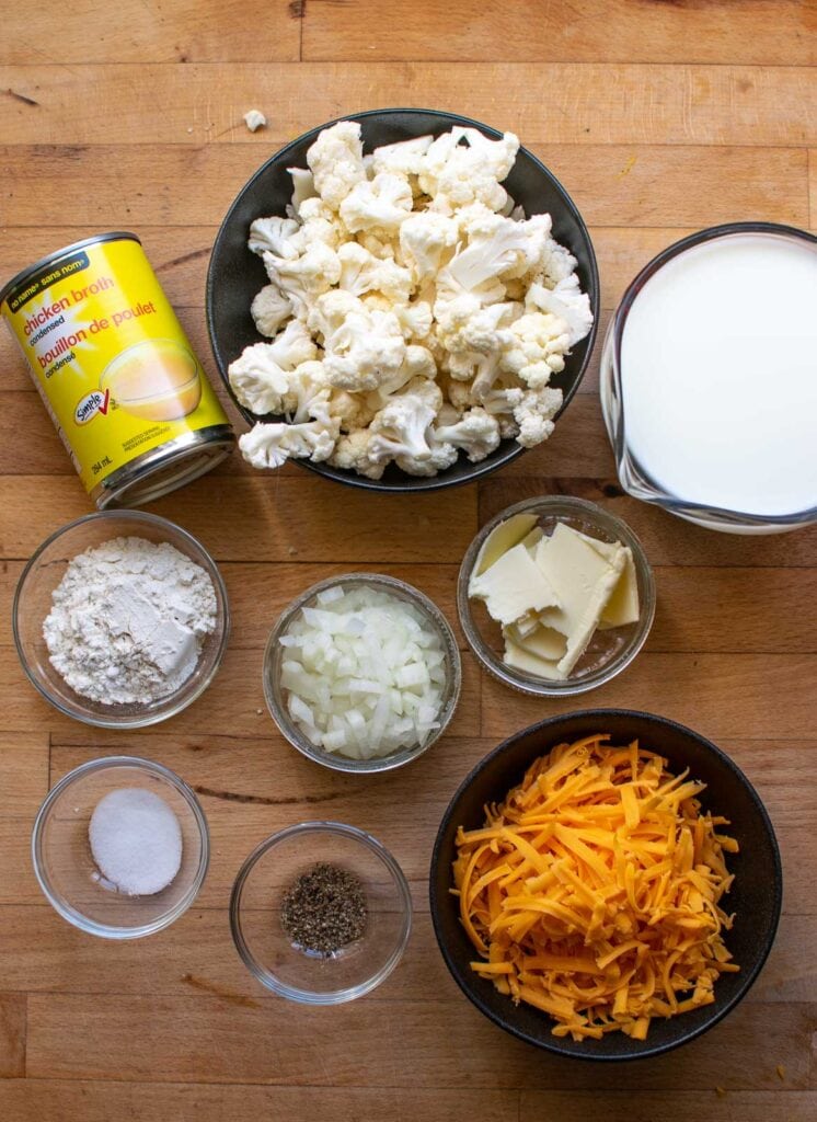 Ingredients to make cauliflower and cheese soup including cauliflower, cheese, chicken broth and onions.