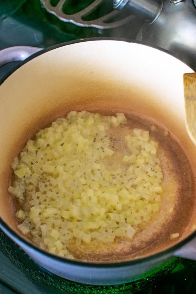 Onions being fried in butter in a dutch oven.