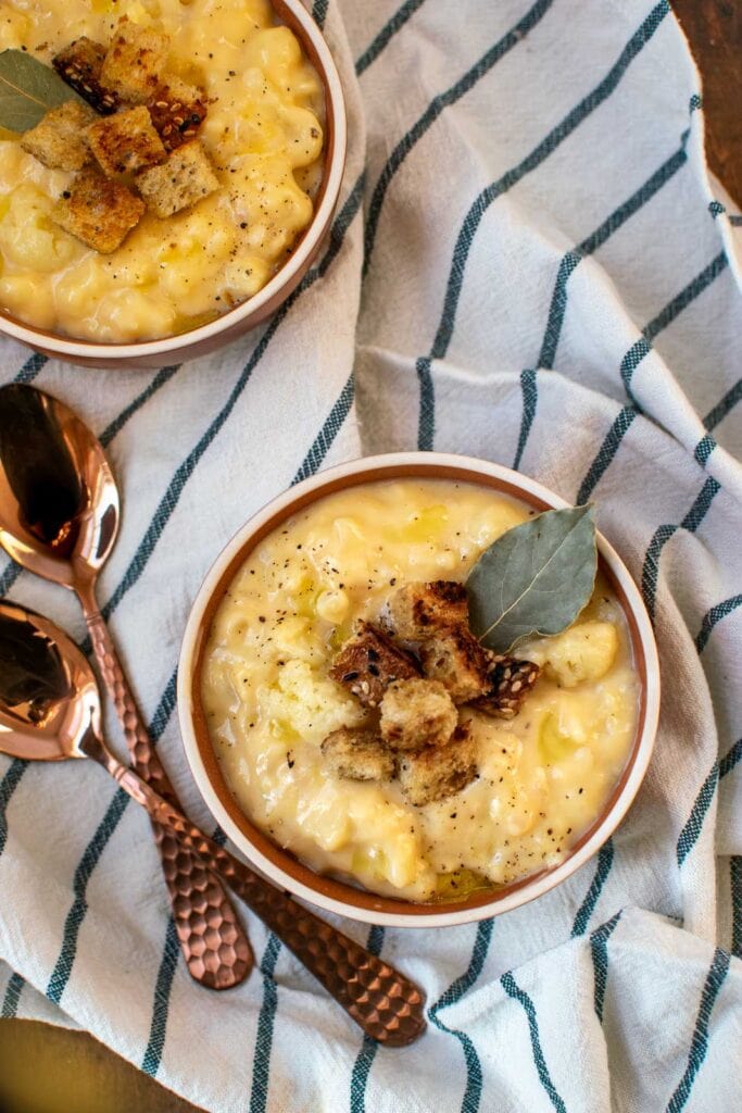Cauliflower cheese soup in small soup bowls and garnished with croutons and a bay leaf.