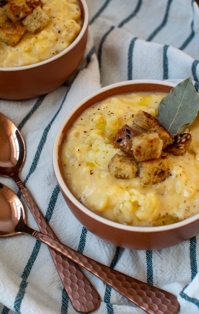 A bowl of cauliflower and cheese soup garnished with mini croutons and a bay leaf.