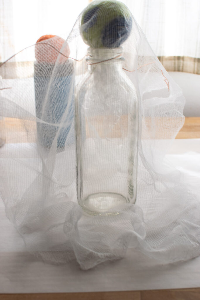 A piece of cheesecloth draped over a milk bottle topped with a ball to make a ghost.