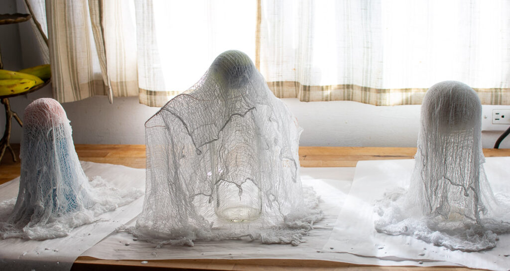 A milk bottle draped with layers of cheesecloth soaked in liquid starch to make a ghost.