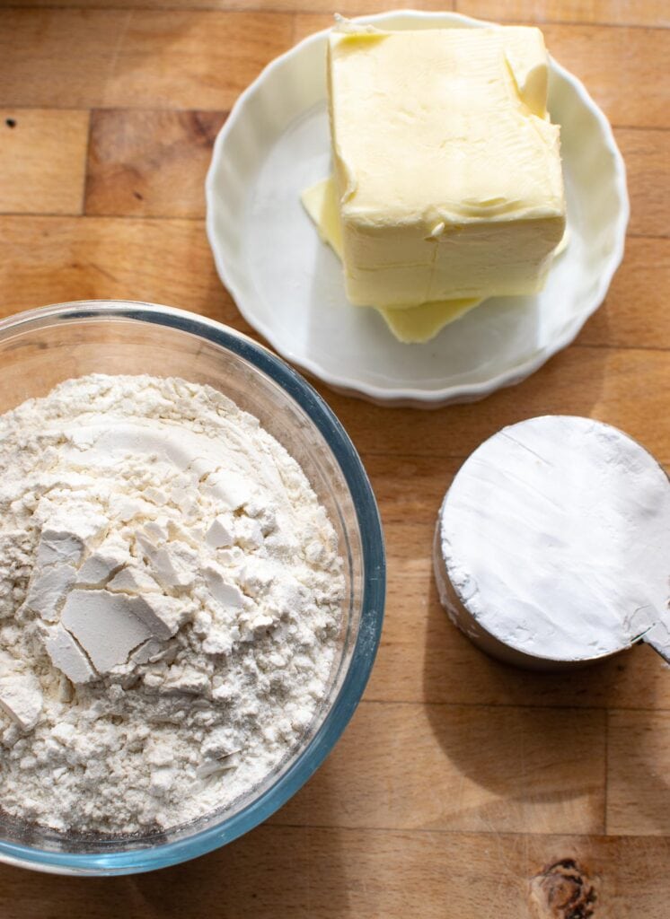 Ingredients to make shortbread cut out cookies including butter, flour and powdered sugar.