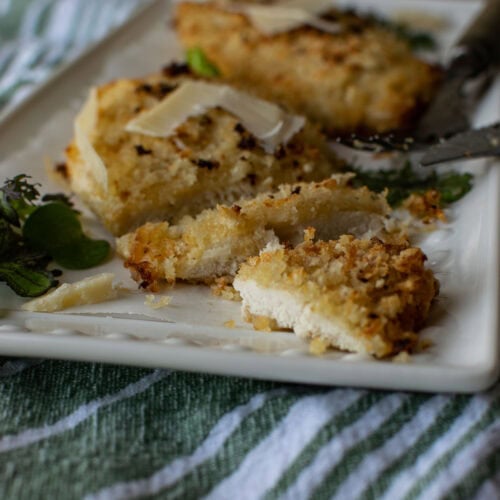 Two pieces of parmesan breaded chicken, one of which is cut in half.