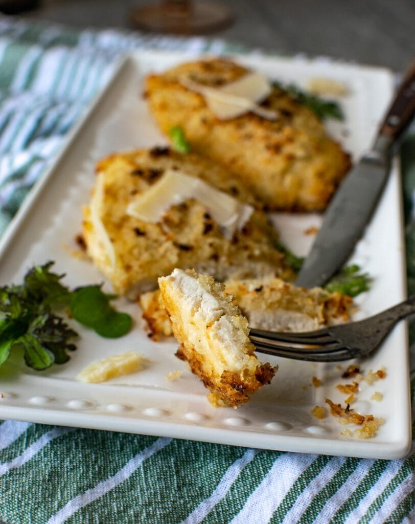 Breaded parmesan chicken slices on a white baking dish.
