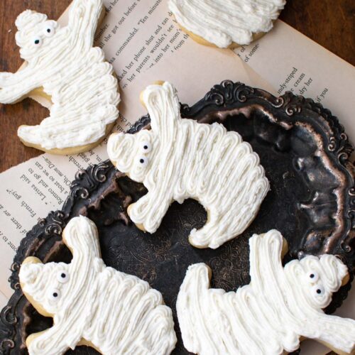 Shortbread cookies cut out into ghost shapes and decorated with white buttercream frosting.