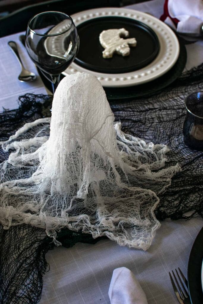 A small cheesecloth ghost on a black spider web table runner.