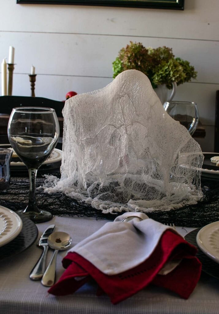 A ghost made of cheesecloth in the centre of a Halloween tablescape.