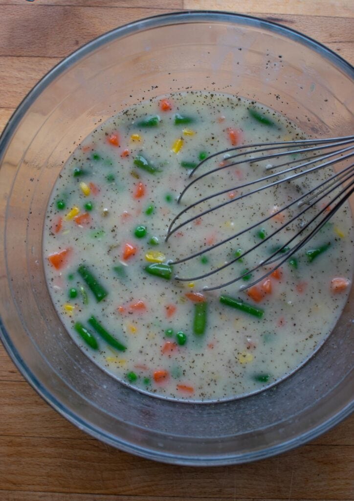 Condensed soup mixed with water, frozen vegetable mixture and long grain rice in a mixing bowl.
