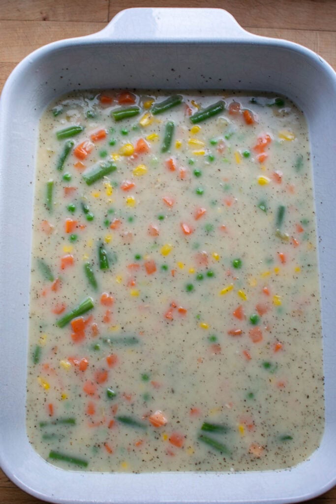 Condensed soup and frozen peas, carrots and corn mixed together with water in a casserole dish.