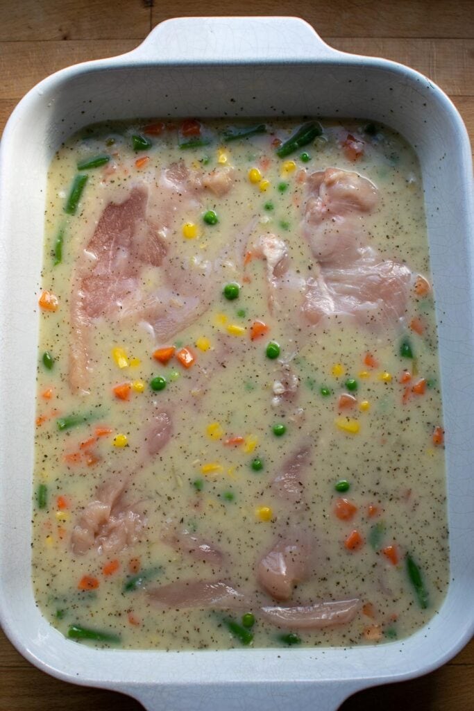 Chicken placed into a casserole dish with a soup and vegetable mixture before baking.