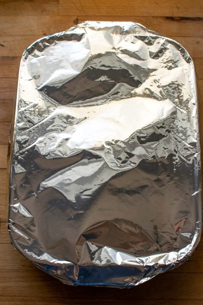 A casserole dish with chicken and rice covered with aluminium foil ready to go into the oven.