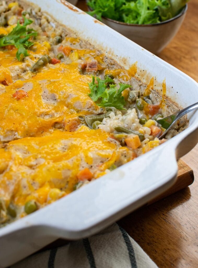 Chicken and rice casserole in a white ceramic dish and a spoon scooping some out.