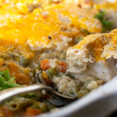 Chicken casserole with rice and vegetables showing a piece of the chicken cut in half after baking and topped with cheese.