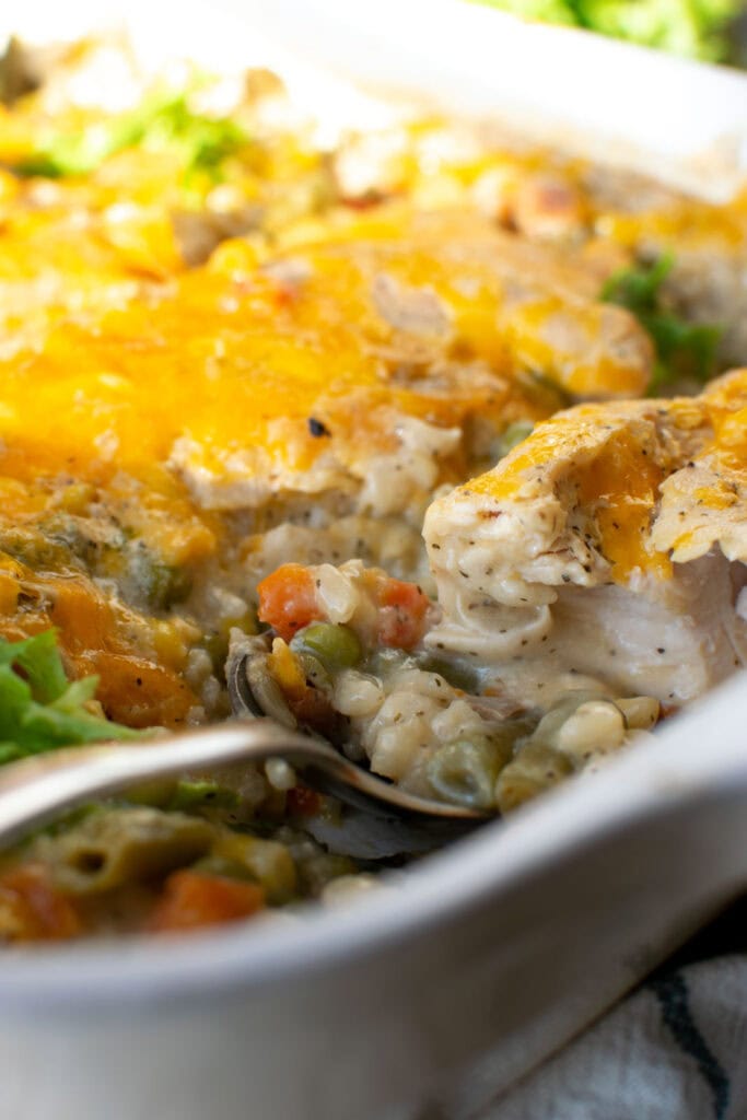 Chicken casserole with rice and vegetables showing a piece of the chicken cut in half after baking and topped with cheese.
