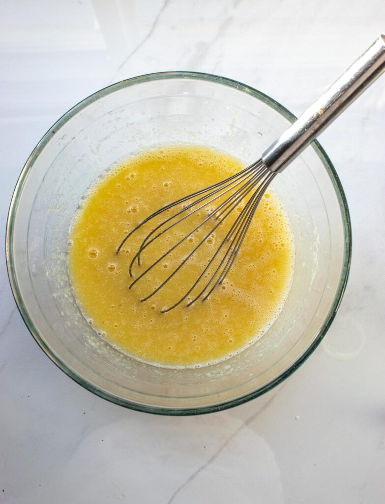 Sugar, applesauce, oil, eggs and milk whisked together in a large glass mixing bowl.