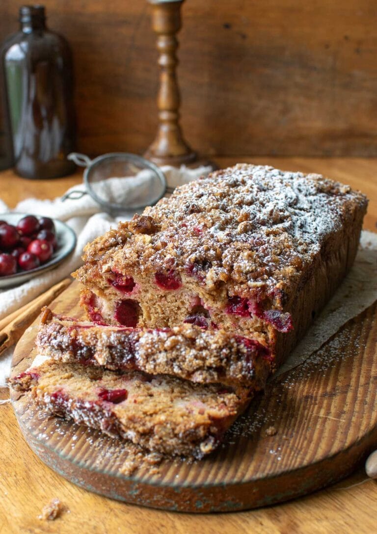 Applesauce cranberry bread on a wood cutting board with 2 slices cut out and laying in front of the loaf to expose all the cranberries inside
