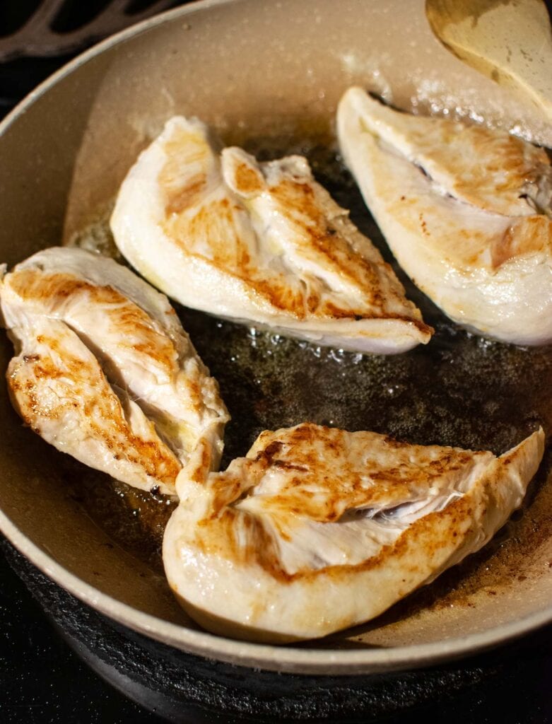 Boneless chicken breast browned in butter in a frying pan.