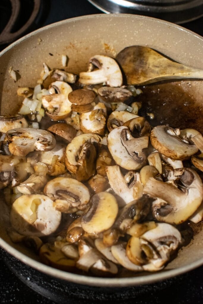 Fresh sliced mushrooms and chopped onions browning in a frying pan.