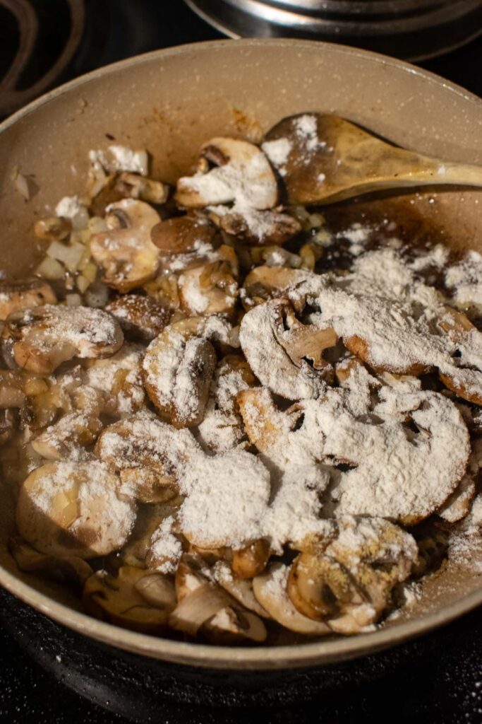 Flour and garlic powder added to mushrooms that have been browned in a frying pan.