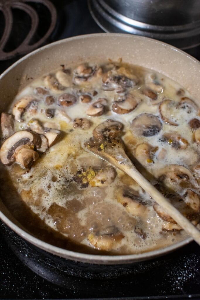 Hot water, Oxo cubes, and cream added to mushroom, onion and flour mixture in a frying pan.