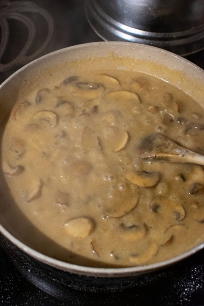 Mushroom and onion cream sauce bubbling and thickening in a frying pan.