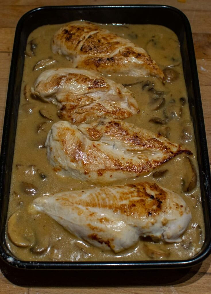 Browned chicken breasts on top of creamy mushroom sauce before baking.