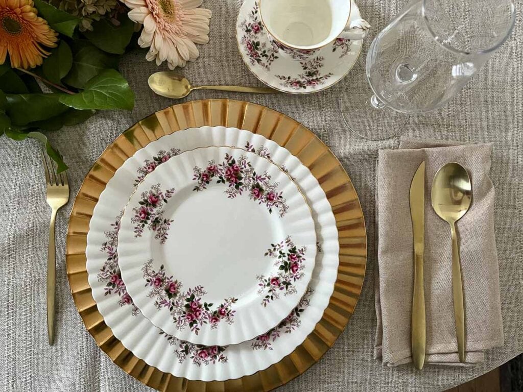 A place setting on a Thanksgiving table with gold charger plate under Royal Albert Lavender Rose china. A teacup and wine glass, and gold flatware complete the setting.