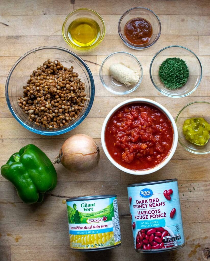 Ingredients to make bean and lentil stew including beans, canned tomatoes, lentils, corn and spices.
