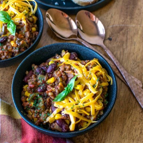 A bowl of meatless stew made with kidney beans and lentils topped with cheddar cheese.