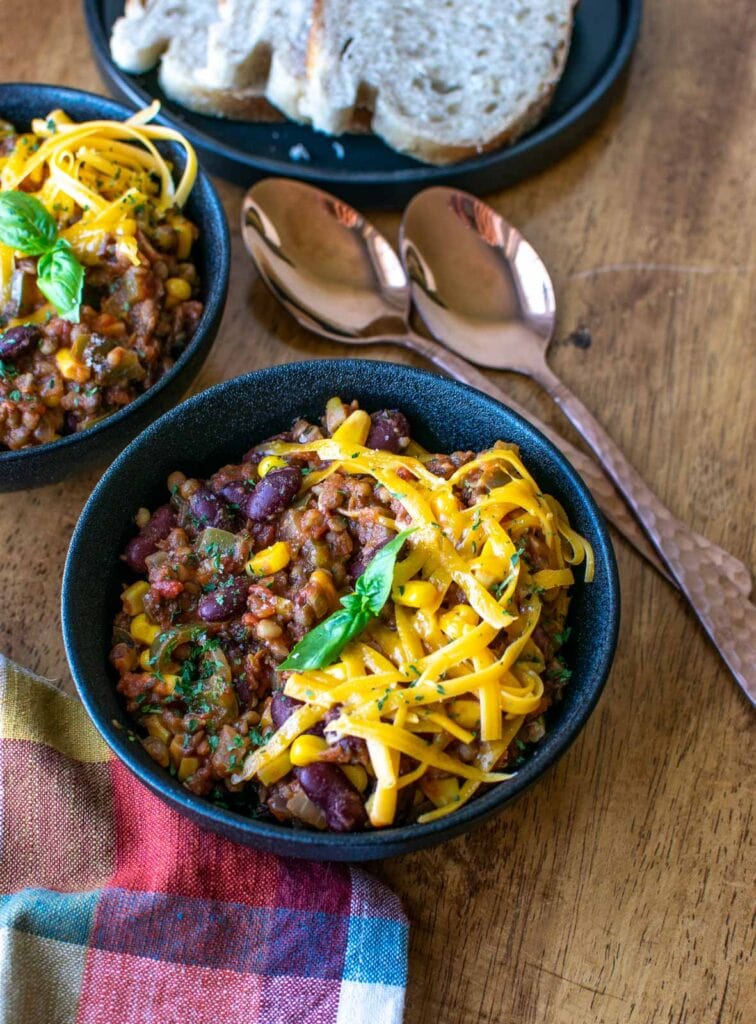 A bowl of meatless stew made with kidney beans and lentils topped with cheddar cheese.