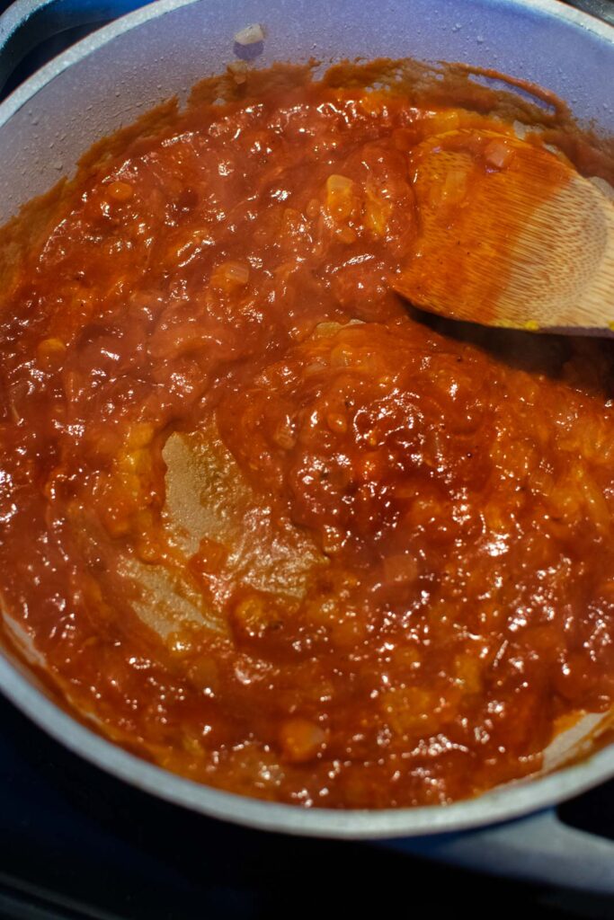 Chili sauce, flour and mustard added to fried onions in a frying pan.