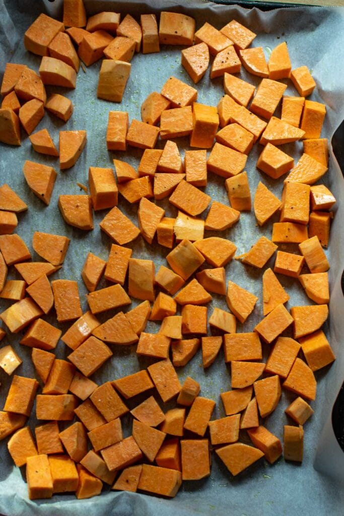 Cubed Sweet potatoes on a parchment lined pan drizzled in olive oil before roasting.