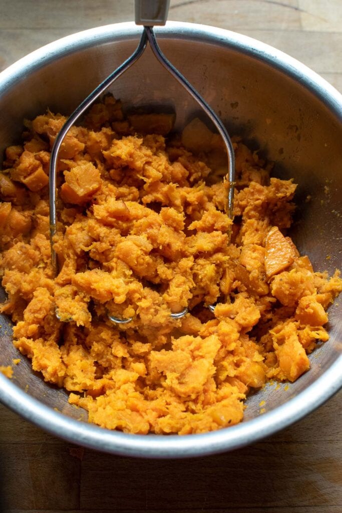 Roasted sweet potatoes being mashed with a potato masher.